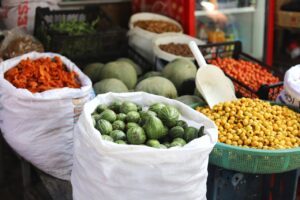 A variety of vegetables and fruits displayed in sacks and baskets at an outdoor market stall.